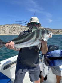 An angler proudly displaying a large Roosterfish while fishing from a boat in a scenic coastal environment.
