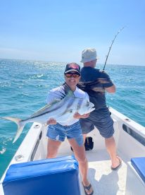 An angler proudly displaying a large Roosterfish while fishing on a boat in clear blue waters.