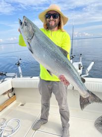 Angler proudly displaying a large Salmon while fishing on a calm day, showcasing the excitement of a successful catch.