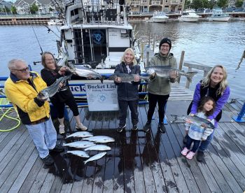 A family proudly displaying their catch of salmon at the dock after a successful fishing trip with Bucket List Fishing Charters.