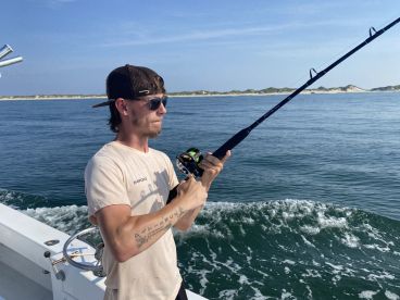 A young angler actively reeling in a catch while fishing off the coast, with a scenic backdrop of calm waters and sandy shores.