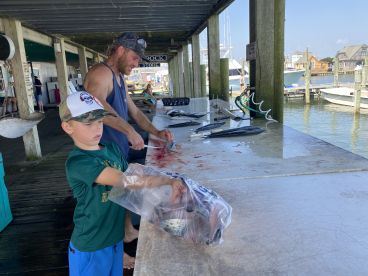A young boy assists with fish preparation at a cleaning station on the dock, showcasing a variety of fish laid out for processing.