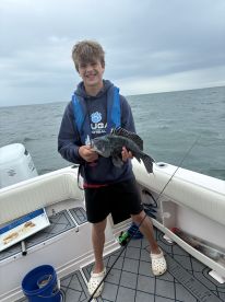A young angler proudly displaying a Black Sea Bass while fishing on a boat, showcasing a successful catch in a coastal environment.