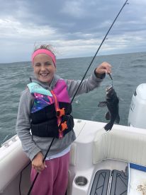 A young angler joyfully displaying her catch, a Black Sea Bass, while fishing on a boat in open waters.