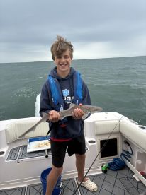 A young angler proudly displaying a caught shark while fishing on a boat, showcasing a fun day on the water.