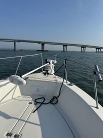 View from the helm of a fishing boat, showcasing the open deck and a bridge in the background, ideal for a day of fishing.