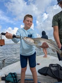A young angler proudly displaying a Speckled Trout while fishing on a boat, showcasing a fun day on the water.