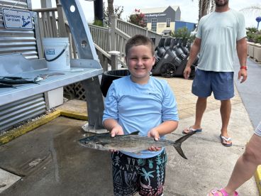 A young angler proudly displaying a caught fish at a cleaning station, with a family member in the background, after a successful fishing trip.
