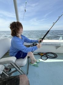 A young angler focused on reeling in a catch while fishing on a boat in open waters.
