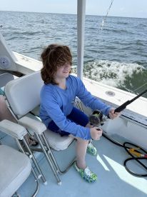 A young angler is actively reeling in a fish while seated on a fishing boat, enjoying a day out on the open water.