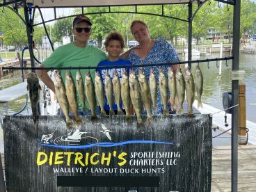 A family proudly displays their catch of Walleye on a board at the dock, showcasing a successful fishing trip with Dietrich's Sportfishing Charters.