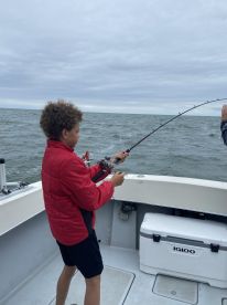 A young angler is actively reeling in a fish while fishing on a boat, showcasing the excitement of the sport in a cloudy ocean setting.