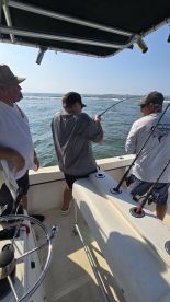 A young angler is reeling in a fish while two adults assist on a fishing charter, enjoying a sunny day on the water.