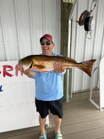 A proud angler displaying a large Redfish at a fishing dock, showcasing a successful day of fishing.