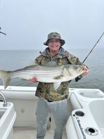 Angler proudly displaying a large Striped Bass while fishing on a boat in overcast conditions.