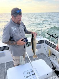 Angler displaying a freshly caught Walleye while fishing on a boat in open waters during sunset.