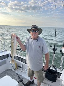An angler proudly displaying a large Walleye while fishing on a boat, showcasing a beautiful sunset backdrop.