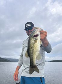 Angler proudly displaying a large Largemouth Bass while fishing on a serene lake, showcasing a successful day on the water.