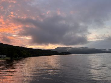 A serene sunset over a calm lake, with misty hills in the background, creating a picturesque fishing environment.