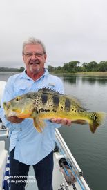 An angler proudly displaying a large Peacock Bass while fishing in a scenic river environment.