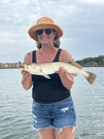 An angler proudly displaying a large Speckled Trout while fishing on a calm day, showcasing the joy of a successful catch.