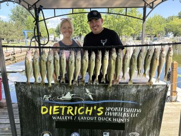 Two anglers proudly displaying a catch of Walleye on a board at a fishing charter dock, showcasing a successful day on the water.