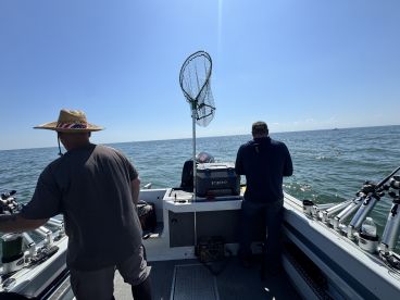 Two anglers aboard a fishing boat, preparing for a day on the water in a sunny environment.