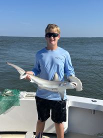 A young angler proudly displaying a caught shark while on a fishing trip, showcasing the excitement of fishing in coastal waters.