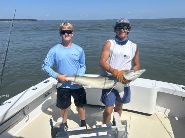 Two young anglers proudly displaying a large shark on a fishing boat, enjoying a day out on the water.