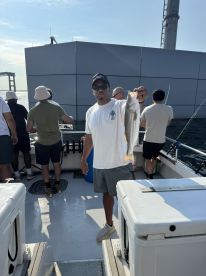 An angler proudly displaying a striped bass while fishing on a charter boat, surrounded by fellow anglers.