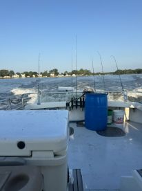 Interior view of a fishing boat cruising on a calm waterway, showcasing fishing rods and a cooler.