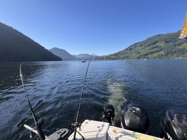 A scenic view of a fishing boat on a calm lake surrounded by mountains, showcasing fishing rods ready for action.