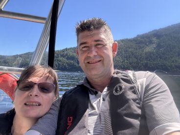 A couple enjoying a sunny day on a fishing boat, surrounded by scenic mountainous views.