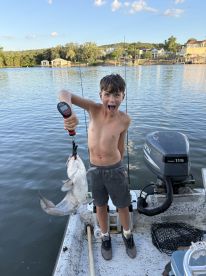 Excited young angler holding a large catfish while fishing from a boat on a scenic lake.