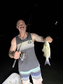 An angler proudly displaying a freshly caught Striped Bass while fishing at night.