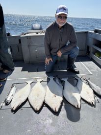 An angler proudly displaying a catch of halibut and other fish on a fishing boat, enjoying a sunny day on the water.