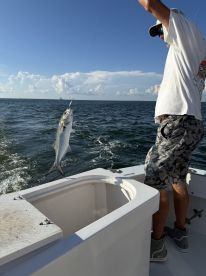 An angler reeling in a Silver King (Tarpon) while fishing on a boat in open waters, showcasing the excitement of the catch.