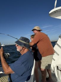 A family enjoying a fishing trip on a boat, with one adult reeling in a catch while a child watches excitedly.