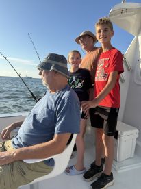 A family enjoying a fishing trip on a boat, with two children smiling and an adult seated, all engaged in the fishing experience.