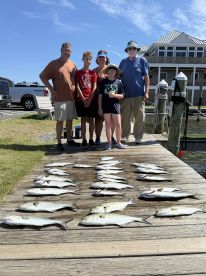 A family poses on the dock with a successful catch of multiple fish, including several species, after a day of fishing.
