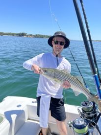 An angler proudly displaying a large Striped Bass while fishing on a sunny day, showcasing the excitement of a successful catch.