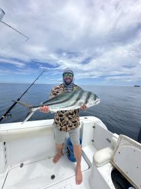 Angler proudly displaying a large Roosterfish aboard a fishing boat in open waters.
