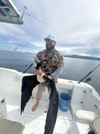 Angler holding a large bird, possibly a pelican, on a fishing boat in calm waters, showcasing an unusual catch during a fishing trip.