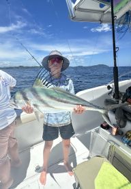 Young angler proudly holding a large Roosterfish on a sunny day while fishing from a boat.
