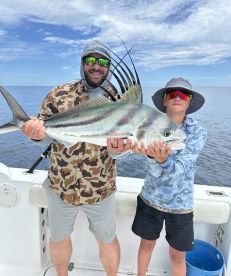 A proud moment as a young angler and an adult display a large Roosterfish while fishing on a boat in open waters.
