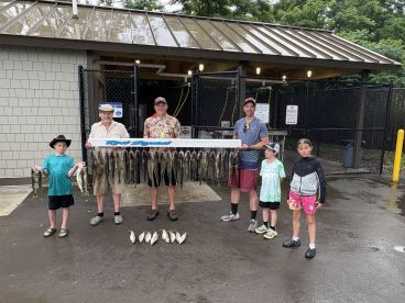 A family group proudly displaying their catch of multiple fish, including catfish, on a catch board at a fishing facility.