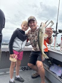 A young angler and an adult proudly displaying a freshly caught Walleye aboard a fishing boat, showcasing a fun family fishing experience.