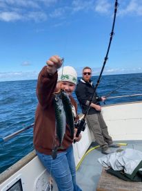 A young angler proudly displaying two Mackerel while fishing on a boat, with a scenic ocean backdrop.