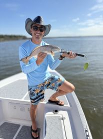 Angler proudly displaying a Redfish while standing on the boat in a sunny fishing environment.