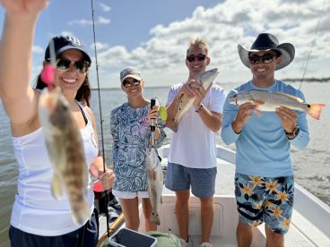 A group of four anglers proudly displaying their catch, including a Redfish and a Speckled Trout, while enjoying a sunny day on the water.